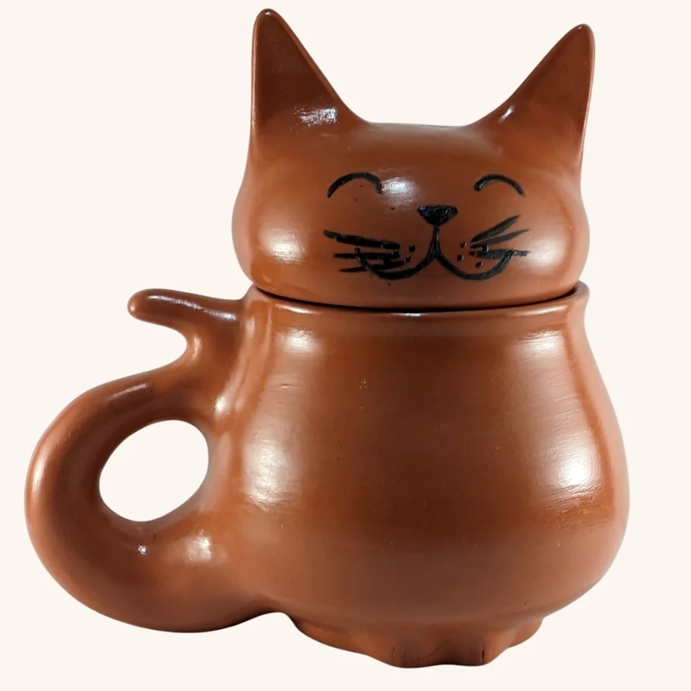 Michi Taza Natural Frente 2025 Michi Tazas, taza en forma de gato panzon hecha a mano en barro rojo y con terminado natural, tiene una tapa con orejitas y carita feliz pintada