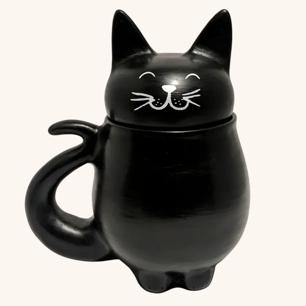 Gato-Negro-Frente-con-Carita.webp Taza negra de gato hecha a mano artesanalmente con tapa en forma de cabeza de gato, tiene orejitas y carita feliz pintada